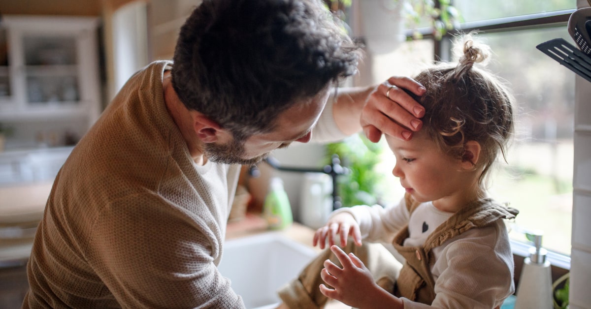 Bambina seduta sul lavello di casa, mentre il pap&agrave; le sente la fronte con la mano per misurare la temperatura